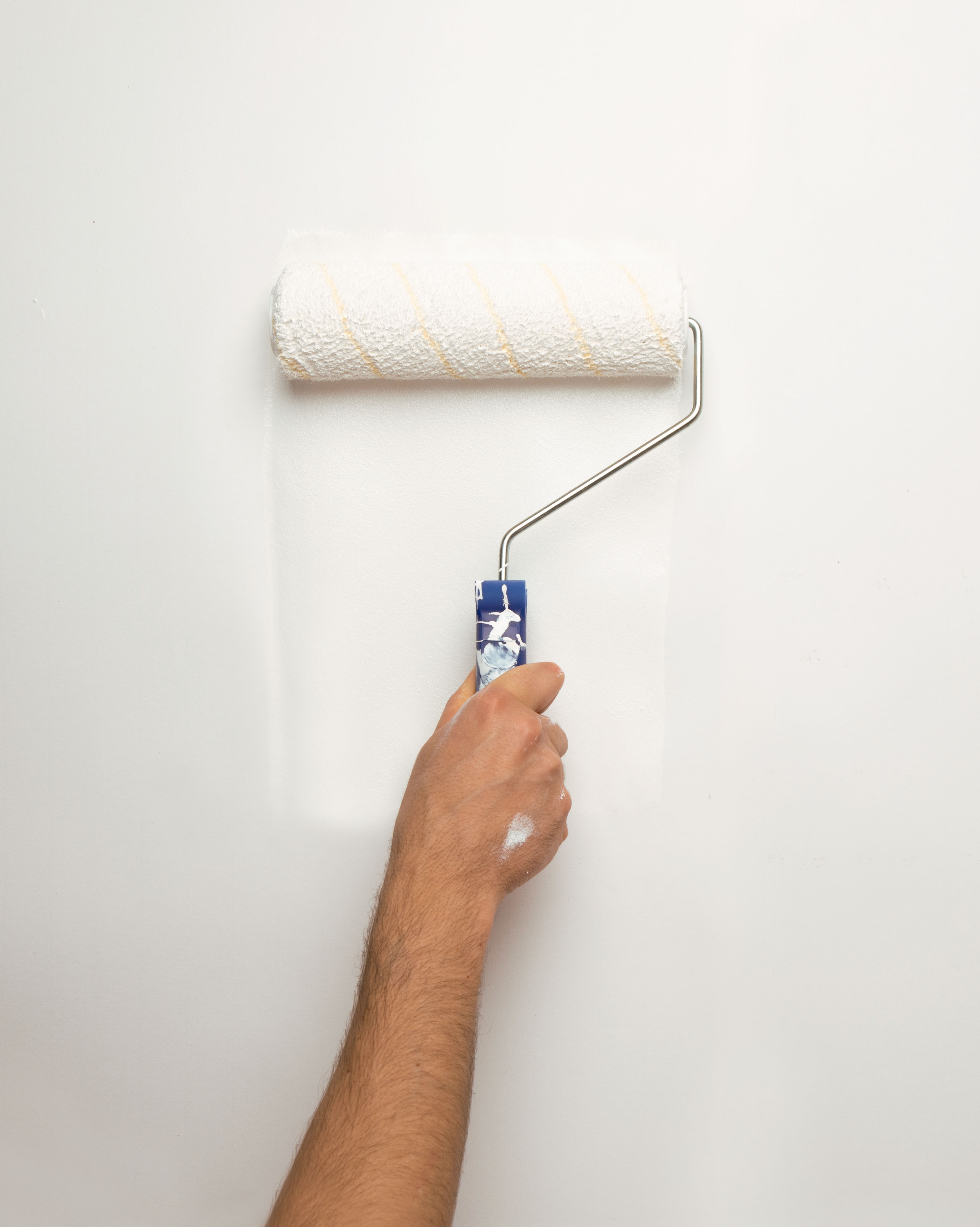 Close-up of a paint roller applying white paint to a wall