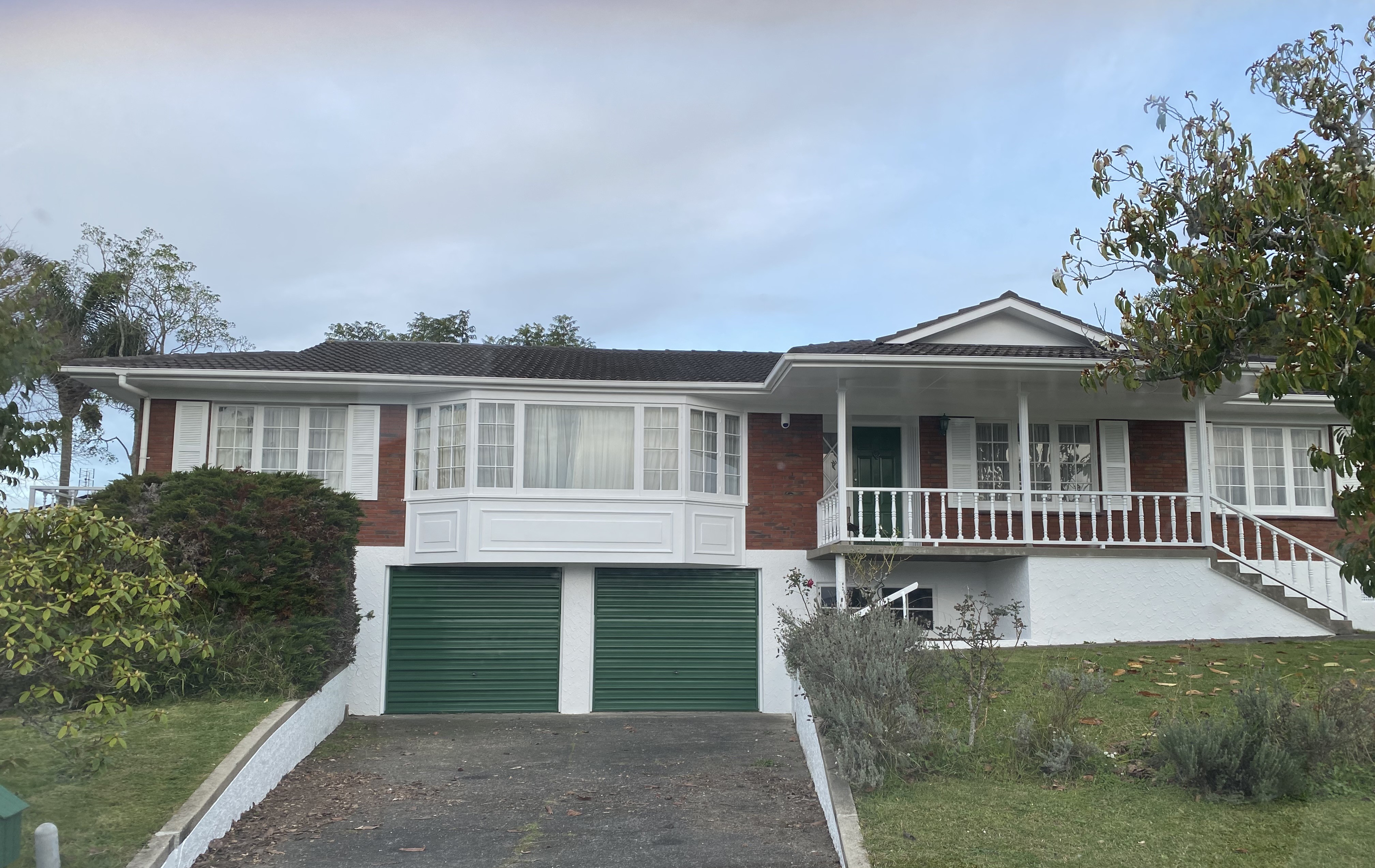Freshly painted residential home exterior — brick and white weatherboard with green garage doors